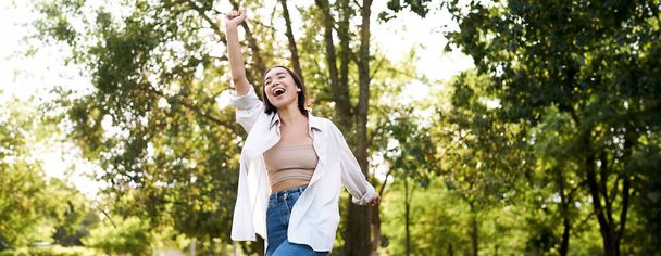 Happy people. Carefree asian girl dancing and enjoying the walk in park, feeling happiness and joy, triumphing. - Фото, изображение
