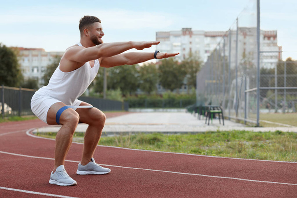 Muscular man doing exercise with elastic resistance band at stadium - Fotoğraf, Görsel