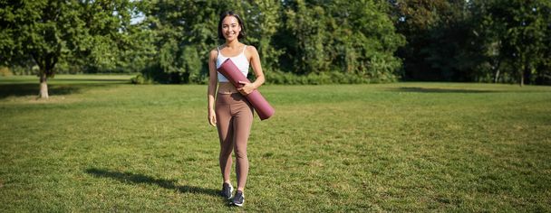 Portré fitness lány séta a parkban gumi jóga szőnyeg, megy a sport edzés a szabadban a gyepen. - Fotó, kép