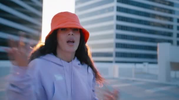 Fancy active young curly multi racial dancer enjoying sunset outdoors on urban city background. Girl in vivid bright orange hat dancing fool around, having fun gesticulating with hands 4K modern RnB - Footage, Video