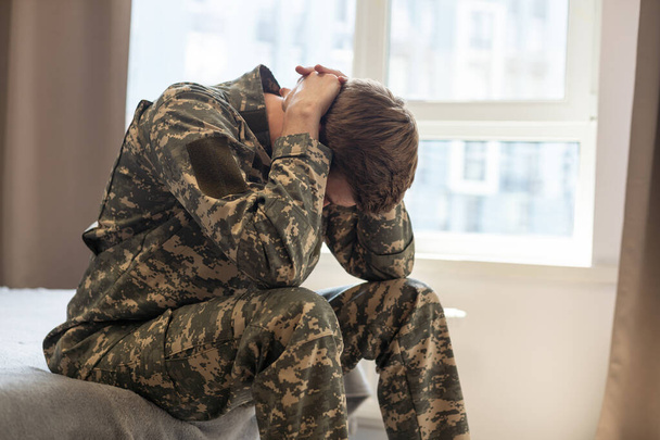 Nervoso masculino militar sofrendo depressão, sentado sozinho em casa, conceito PTSD
 - Foto, Imagem