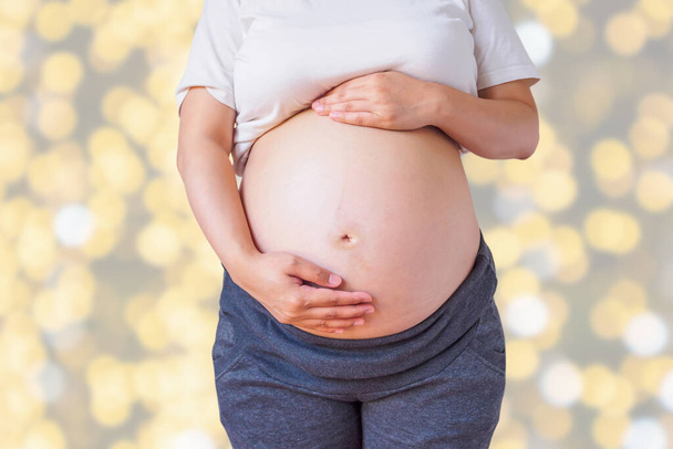 schwangere Frau hält ihren Schwangerschaftsbauch über Urlaub Bokeh Lichter Hintergrund - Foto, Bild