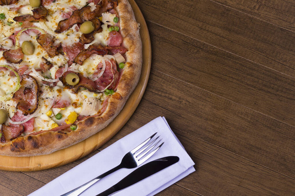 Portuguese pizza made with ham, pea egg, heart of palm, pepperoni, onion and mozzarella and bacon. Served on wooden board. Top close-up photograph. - Photo, Image