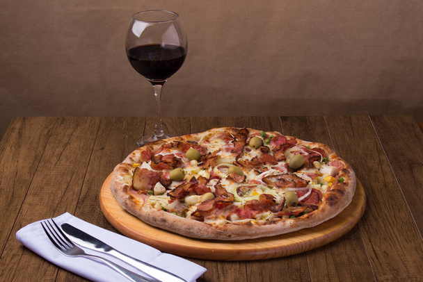 Portuguese pizza made with ham, pea egg, heart of palm, pepperoni, onion and mozzarella and bacon. Glass of red wine. Gastronomic photography. - Photo, Image