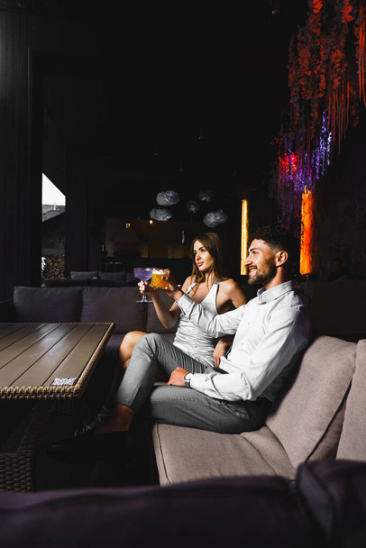 Un couple amoureux boit un cocktail et fume un narguilé sur la terrasse la nuit. Concept de vie nocturne - Photo, image