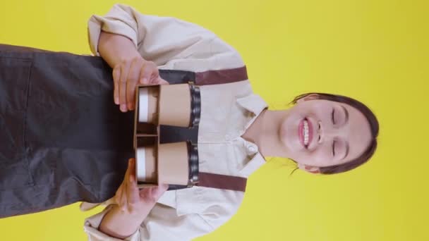 Portré fiatal ázsiai barista nő visel kötény ad kávéscsésze sárga háttér, pincérnő vagy vállalkozó gazdaság kávé izgatott, kisvállalkozás vagy startup, pincér kávézó. - Felvétel, videó