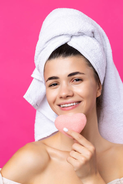 Hermosa chica atractiva alegre con una toalla en la cabeza, sostiene una esponja en forma de corazón rosa. - Foto, imagen
