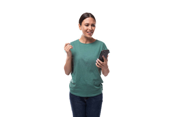 well-groomed slim young brunette woman dressed in a green t-shirt with surprise holding a smartphone. - Photo, Image