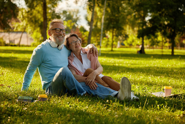 Glücklich verliebtes romantisches Paar, das sich umarmt, während es sich auf dem Rasen im Park ausruht. Entspannte reife Eheleute, die sich umarmen und romantische Stimmung verbreiten - Foto, Bild