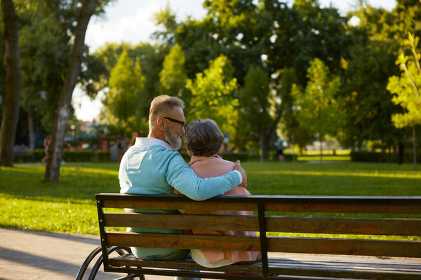 Boldog pár élvezi a nyugalmat és idilli hangulatot a nyilvános parkban, miközben ül a padon. Kilátás hátulról vidám szerető férfi és nő, amelynek romantikus dátum - Fotó, kép