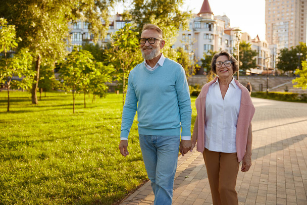 Счастливая пожилая пара туристов, гуляющих среди общественного парка на экскурсии, наслаждаясь веселым времяпрепровождением вместе и захватывающим приключением в чужой стране - Фото, изображение