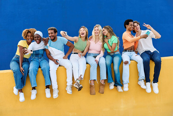 Grupo de personas milenarias usando el teléfono sentado en una pared colorida - Foto, Imagen