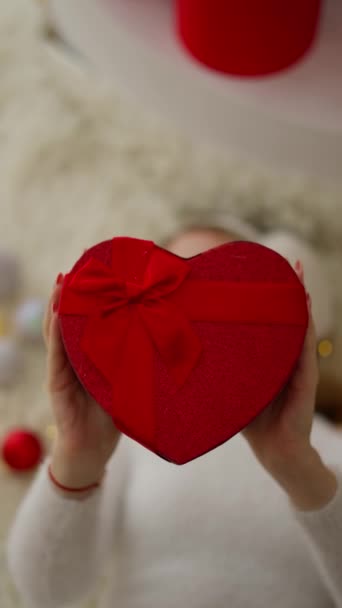 Egy gyönyörű szőke nő mosolyog és egy szív alakú dobozt tart Valentin napra. - Felvétel, videó