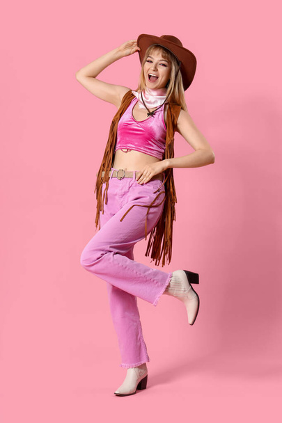 Молодая женщина, одетая как ковбойша кукла на розовом фоне - Фото, изображение
