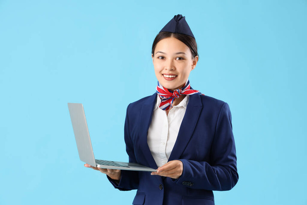 Красивая азиатская стюардесса с ноутбуком на синем фоне - Фото, изображение