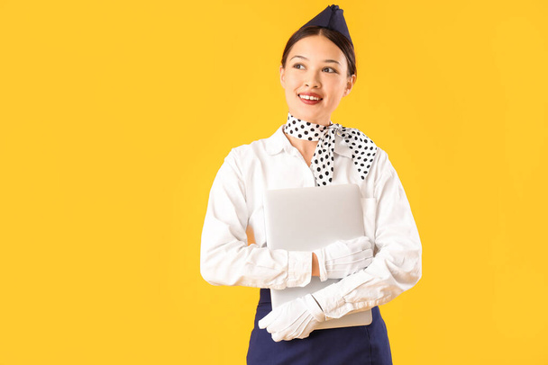 Bella hostess asiatica con laptop su sfondo giallo - Foto, immagini