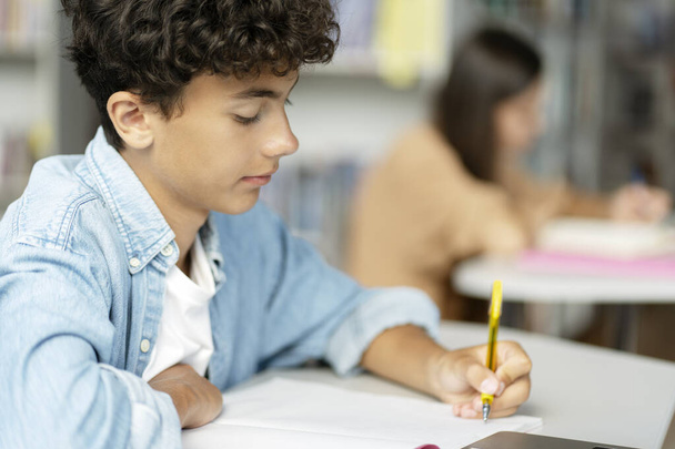 Sprytny nastolatek robi notatki, uczy się języka, przygotowuje egzaminy, czyta książki w nowoczesnej klasie. Powrót do szkoły, koncepcja edukacji  - Zdjęcie, obraz