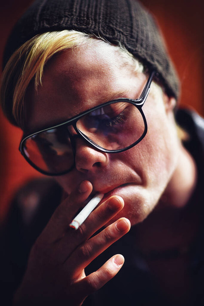 Face, addiction and a boy smoking a cigarette closeup for nicotine or tobacco dependency in sunglasses. Style, smoke and bad habit with a young person inhaling an addictive substance for cancer. - Photo, Image