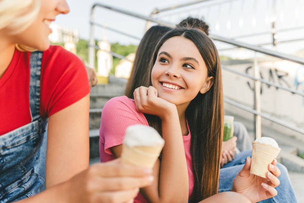 Portret uśmiechniętych wielorasowych nastolatków, dzieci, jedzących lody, smaczny deser, spacerujących razem po miejskiej ulicy. Atrakcyjne, młode dziewczyny rozmawiające, komunikacyjne, wakacyjne. Koncepcja przyjaźni - Zdjęcie, obraz
