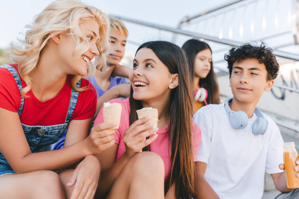 Bir grup gülen arkadaş, dondurma yiyen, dışarıda oturmuş limonata içen çok ırklı gençler. Sokaktaki şık erkek ve kız muhabbetiniz kutlu olsun. Arkadaşlık, pozitif yaşam tarzı, yaz.  - Fotoğraf, Görsel