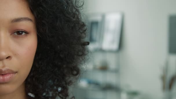 People close up half face portrait of calm relaxed young multi racial curly model. Pretty mixed race girl no facial expression looking straight to camera in modern apartment on blurred copy background - Footage, Video
