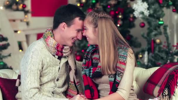 Szerető pár öltözött pulóvert és sálat gazdaság ajándékokat egy karácsonyi berendezett szobában. Fiatal pár szerelmes ember, és csinos lány visel pulóvert és sálat otthon. - Felvétel, videó