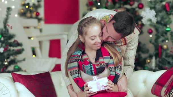 Любящая пара, одетая в свитер и шарф с подарками в рождественской комнате. Молодая пара влюблённых мужчин и красивая девушка в свитере и шарфе дома
. - Кадры, видео