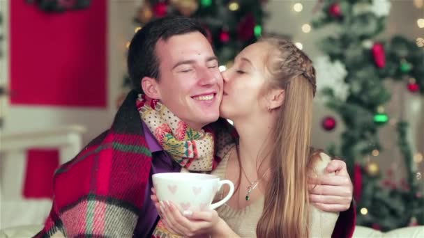 Casal amoroso vestido com suéter e lenço segurando presentes em uma sala mobilada de Natal. Jovem casal no homem de amor e menina bonita vestindo suéter e cachecol em casa
. - Filmagem, Vídeo