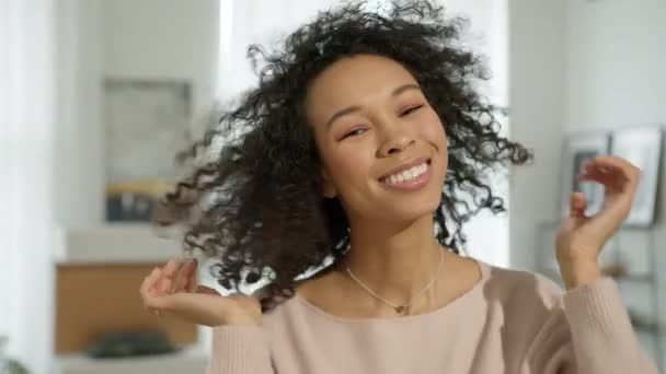 Woman with beautiful curly hair slow mo, Fun happy young girl shake head to make afro hair flying. Attractive gorgeous young biracial elegant lady looks into camera at modern apartment on background - Footage, Video