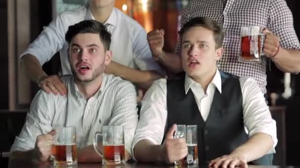 Vier befreundete Geschäftsleute trinken Bier und jubeln und schreien gemeinsam vor dem Fernseher an der Bar. Freunde erfolgreicher Geschäftsleute amüsieren sich gemeinsam in der Bar bei einem Bier vor dem Fernseher. - Filmmaterial, Video