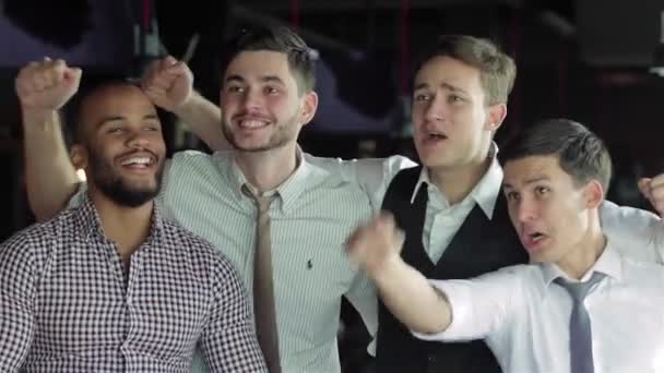 Vier befreundete Geschäftsleute trinken Bier und jubeln und schreien gemeinsam vor dem Fernseher an der Bar. Freunde erfolgreicher Geschäftsleute amüsieren sich gemeinsam in der Bar bei einem Bier vor dem Fernseher. - Filmmaterial, Video
