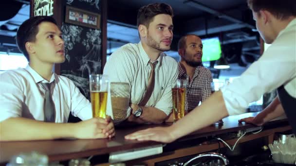 Cuatro amigos hombres de negocios beben cerveza y se regocijan y gritan juntos viendo la televisión en el bar. Exitosos hombres de negocios amigos divirtiéndose juntos en el bar con una cerveza viendo fútbol en la televisión
. - Metraje, vídeo
