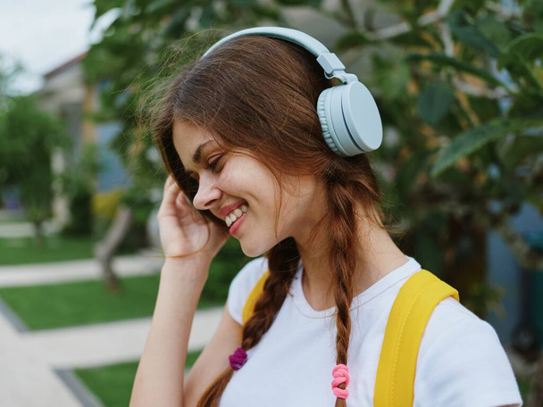 Mujer joven retrato felicidad viaja de vacaciones con una mochila amarilla y auriculares escuchando música con una sonrisa caminando fuera. Foto de alta calidad - Foto, Imagen