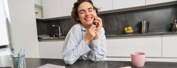 Portret van schattig lachend meisje praat op mobiele telefoon, zit thuis en belt iemand met smartphone. - Foto, afbeelding