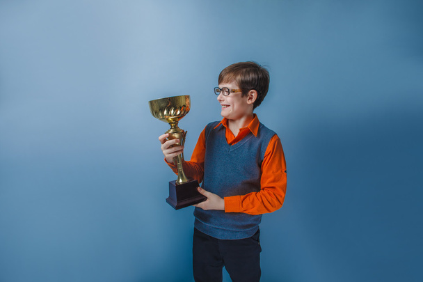 European-looking boy of ten years in glasses holding a cup award on a blue background - Photo, Image
