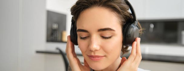 Nahaufnahme Porträt einer Frau Gesicht, Musik hören in ihren drahtlosen Kopfhörern mit Freude und Vergnügen, genießen gute Klangqualität in Kopfhörern. - Foto, Bild