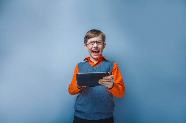 Európai-látszó fiú tízéves szemüveg tabletta tartja a kezében a kék háttér - Fotó, kép