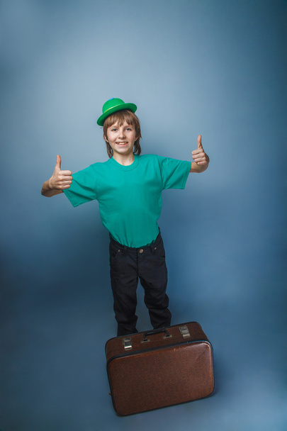 帽子のスーツケースを手で保持している青色の背景に旅程で 10 年間のヨーロッパ見て少年 - 写真・画像