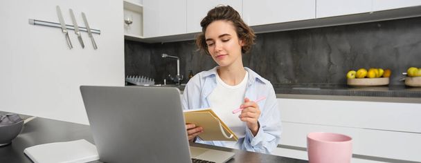Робоча жінка робить нотатки, записує інформацію на ноутбук, сидячи з ноутбуком вдома. - Фото, зображення