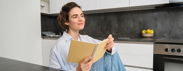 Portrait of young adult woman, reading her notes, holding notebook and smiling, relaxing at home. - Foto, immagini