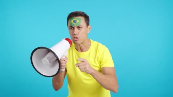 Відео в студії з хромою чоловіка з бразильським прапором, намальованим на його обличчі, що об'єднує натовп за допомогою мегафона - Кадри, відео