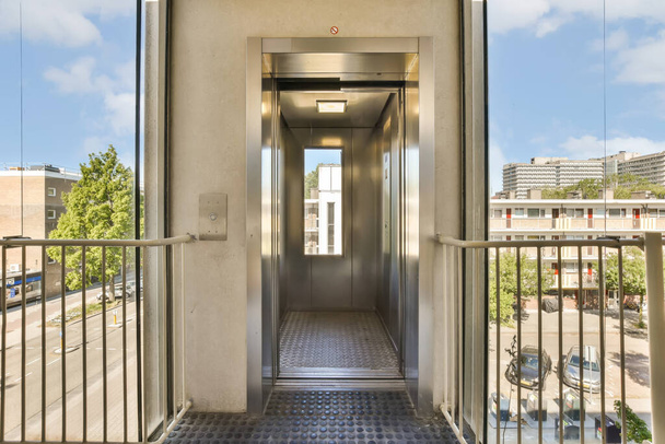 ένα ασανσέρ σε ένα κτίριο με μπλε ουρανό και λευκά σύννεφα πίσω από τις πόρτες είναι ανοικτές για να επιτρέψει την πρόσβαση για τους ανθρώπους - Φωτογραφία, εικόνα