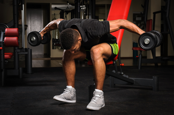Young man doing Seated Bent Over Dumbbell Reverse Fly workout in gym - Foto, Bild