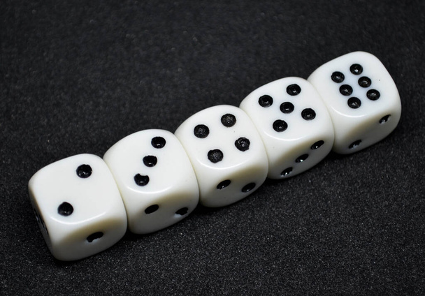 Los dados blancos son pequeños, accesorios de juego en forma de cubo, sobre fondo negro, tienen blackpips en cada cara, se utilizan comúnmente en varios juegos de mesa. - Foto, imagen