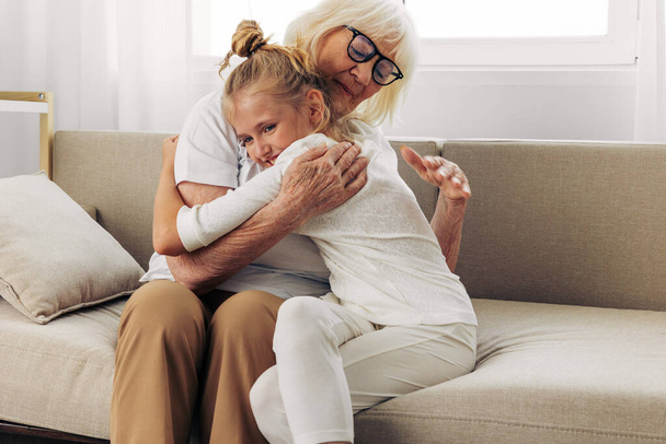 Ζωή γυναίκα κόρη γιαγιά αγκαλιάζει κορίτσι συγκόλληση καναπέ μητέρα αγκαλιά γενιά καθιστικό καναπέ μεγαλύτερο παιδί ευτυχισμένη εγγονή οικογένεια ηλικιωμένοι αγάπη σπίτι παλιά - Φωτογραφία, εικόνα