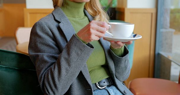 Frau blickt auf Fenster im Café und trinkt Kaffee aus weißer Tasse. Bussines Frau beim Kaffee zum Mittagessen. Hochwertiges Foto - Foto, Bild