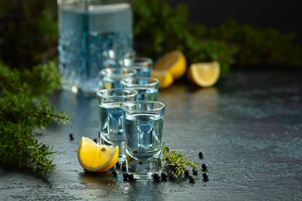 Синий джин и можжевельник на старом темно-синем столе. Джин с ягодами можжевельника и ломтиками лимона. - Фото, изображение