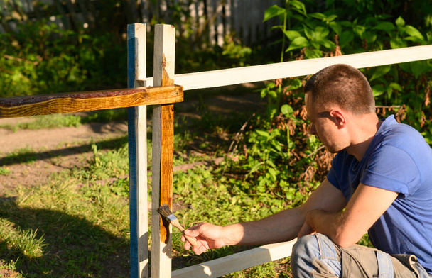 Un homme en plein air peignant du bois avec un pinceau. par une belle journée ensoleillée dans le jardin - Photo, image