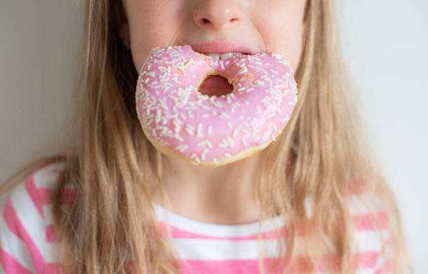 Kleines blondes Mädchen isst köstlichen Donut im Haus  - Foto, Bild