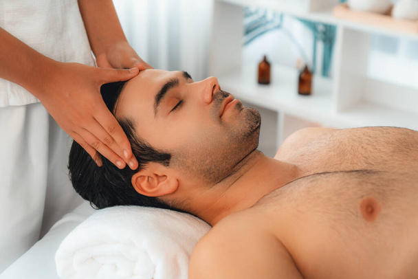 Kaukaski mężczyzna korzystających relaksujący antystresowy masaż głowy i rozpieszczające piękno twarzy rekreacji rekreacji skóry w dayspa nowoczesne światło ambient w luksusowym ośrodku lub hotelowym salonie spa. Cichy zapach - Zdjęcie, obraz
